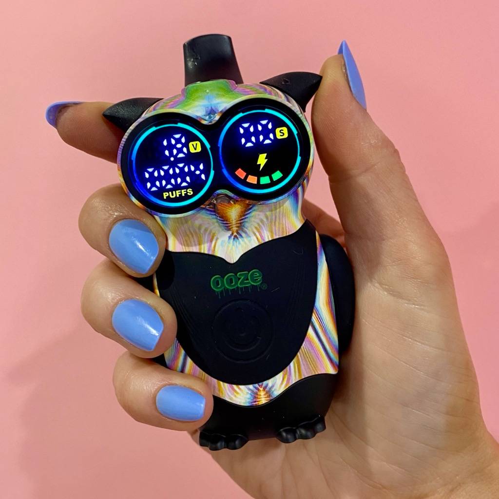 Close up of a hand holding the glitch Ooze Hoot Owl character vape battery against a light pink background