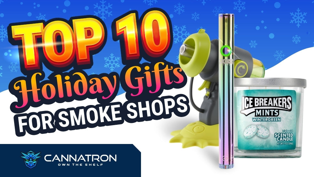 An elf on the shelf doll with an Ooze shirt is in a Christmas tree with turquoise and green ornaments and silver ribbon. He has a rainbow Ooze slim twist vape pen.