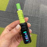 A hand holding a black Ooze Runt Mini Battery device with a bright lime green textured grip and a matching green mouthpiece, set against a gray and green carpeted floor.
