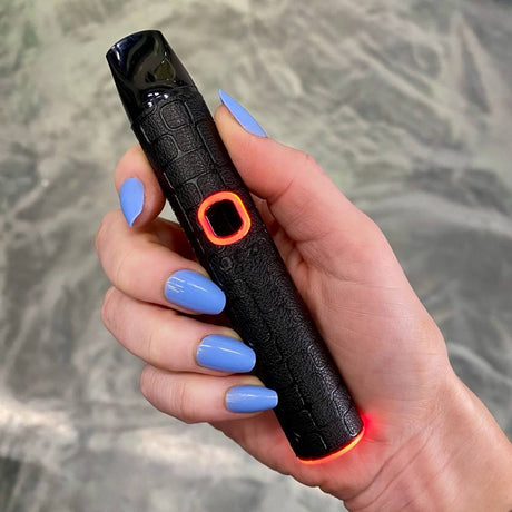 Hand holding a black Ooze Pinch dry herb device with a textured grip, against a neutral background.