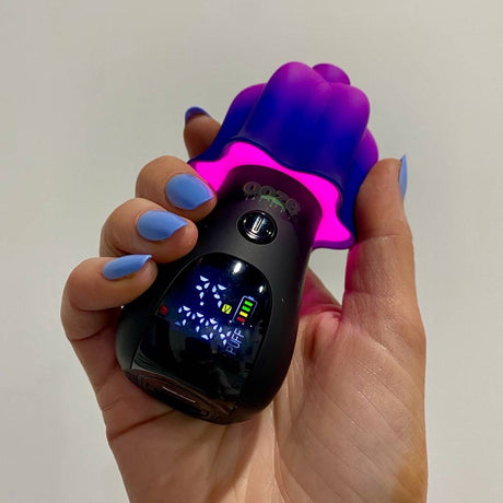 Hand holding a purple and black Ooze Shroom character vape device with digital display and pink LED lights under the mushroom cap