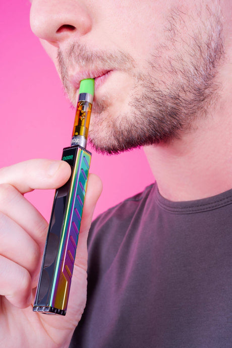 Close up of a person hitting a rainbow Ooze Quad 2 square vape pen against a bright pink background
