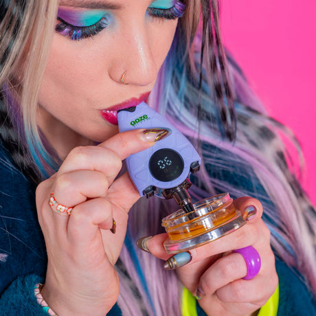 Person using a purple Ooze Hover dab straw with a pink background
